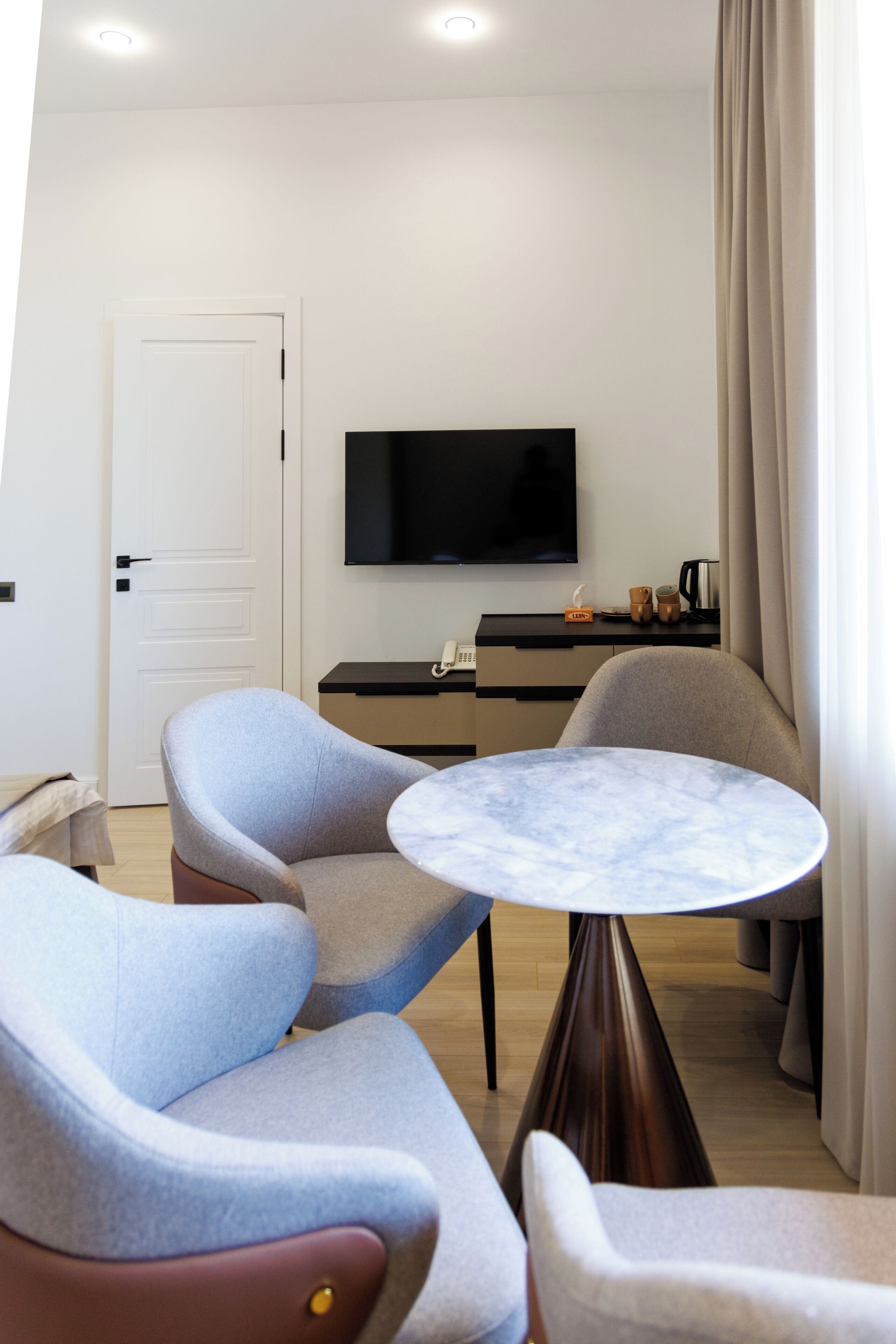 Una habitación de hotel moderna con un televisor de pantalla plana, una mesa redonda de mármol y dos sillones.