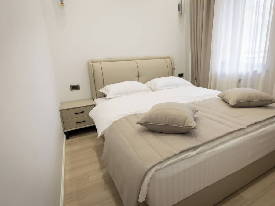 A neatly made bed with a headboard, two pillows, and a bedside table with drawers.
