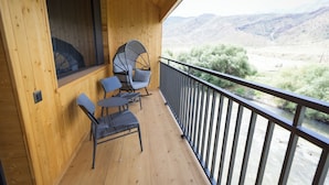 Un balcone in legno con vista su un fiume e delle colline.