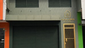 Un edificio de dos pisos con fachada verde, una puerta de garaje cerrada y un letrero que indica 'CASA LUMEN EST. 2024'.