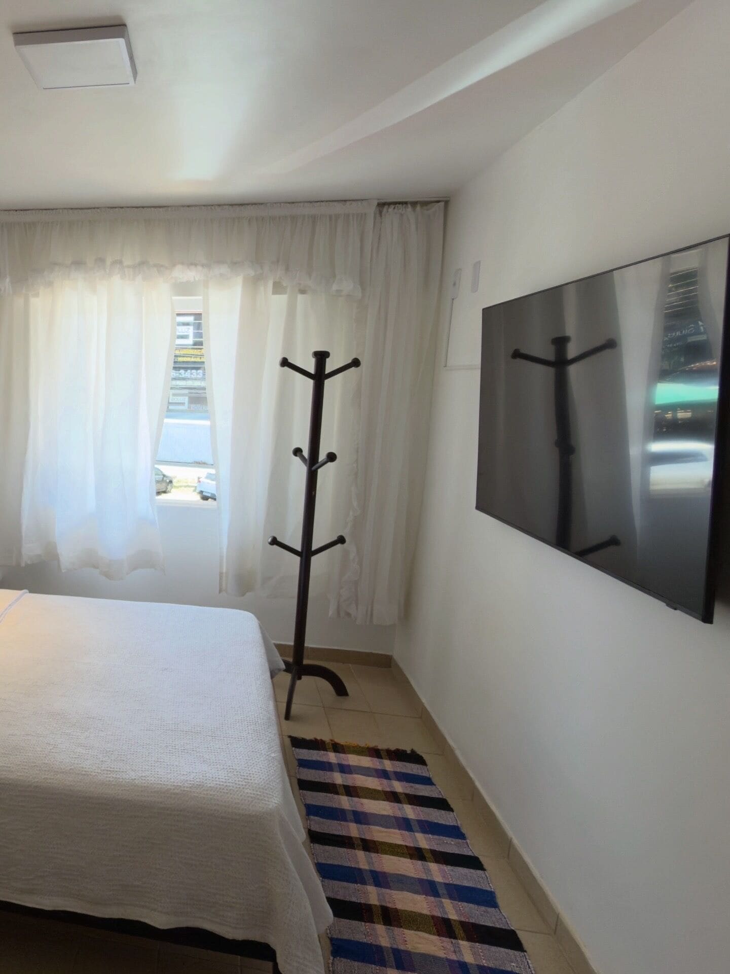A hotel room with a bed, a coat rack, a television, and a window with curtains.