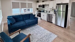 Een moderne keuken met witte kastjes, roestvrijstalen apparatuur en een blauwe bank in de woonkamer.