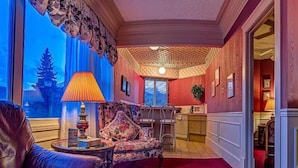 A room with a red carpet, a leather sofa, a small table with a lamp, and a view of the outdoors. - The Athabasca Hotel (JASPER)