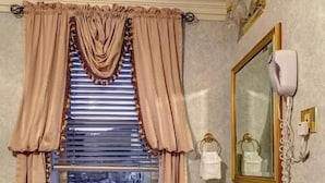 A bathroom with a pedestal sink, a window with curtains, a mirror, and a telephone. - The Athabasca Hotel (JASPER)
