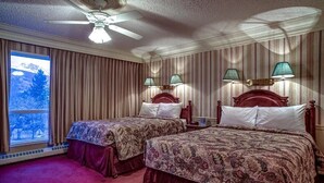 A hotel room with two beds, a ceiling fan, a window with a view, and wall-mounted lamps. - The Athabasca Hotel (JASPER)