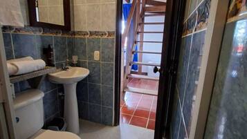 A bathroom with a toilet, sink, and mirror. There is a door leading to a staircase.