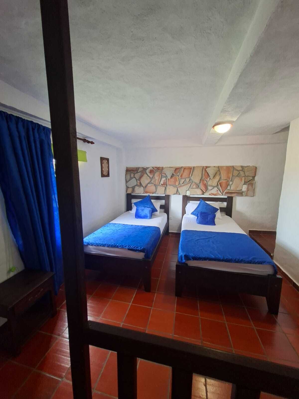 Una habitación con dos camas, una pared de piedra y un suelo de baldosas rojas.
