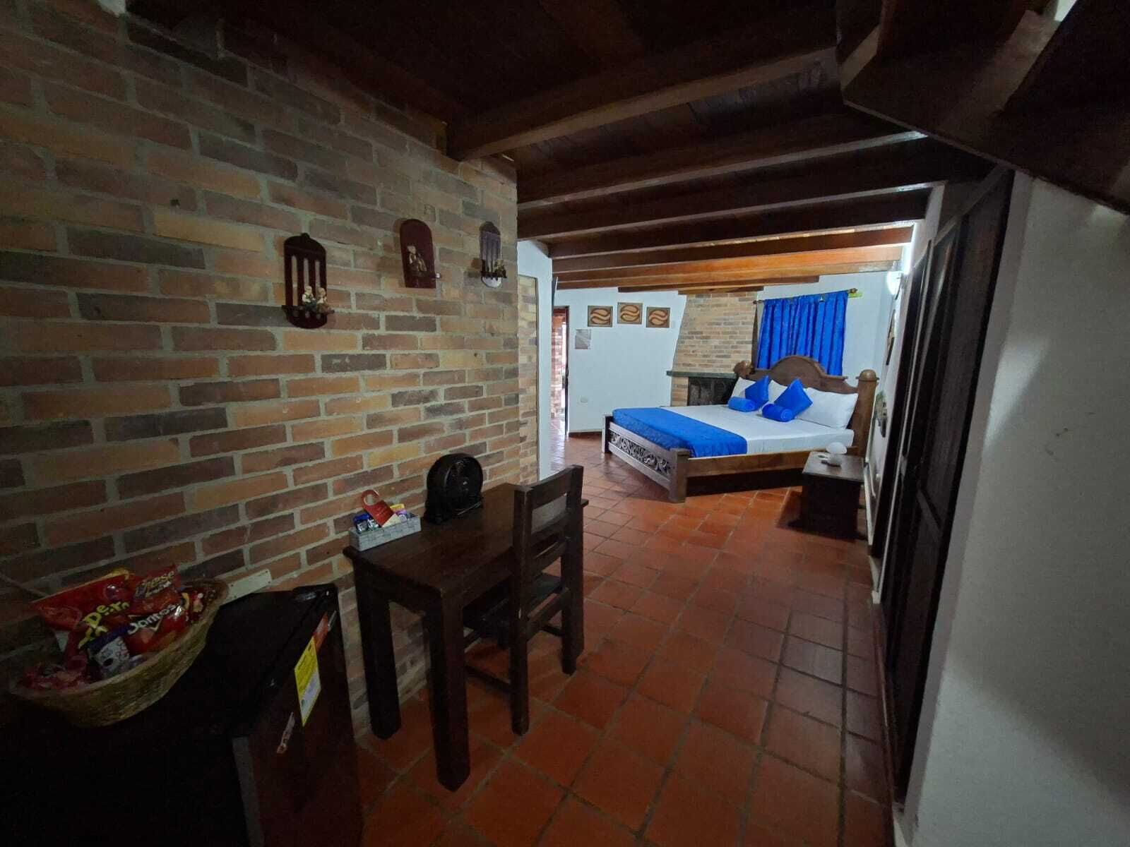A room with a brick wall, a bed with blue bedding, a wooden chair, and a small table with snacks.