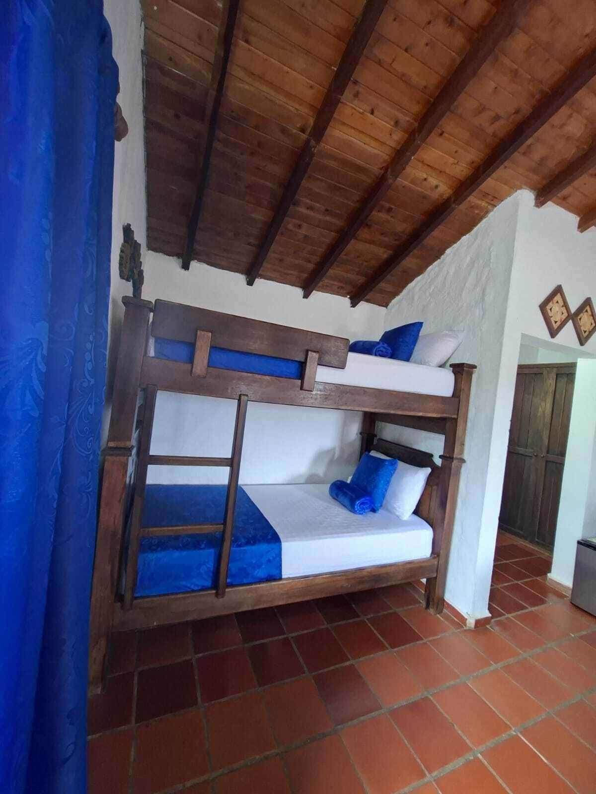 Un llit superposat amb estructura de fusta, roba de llit blanca i detalls blaus.