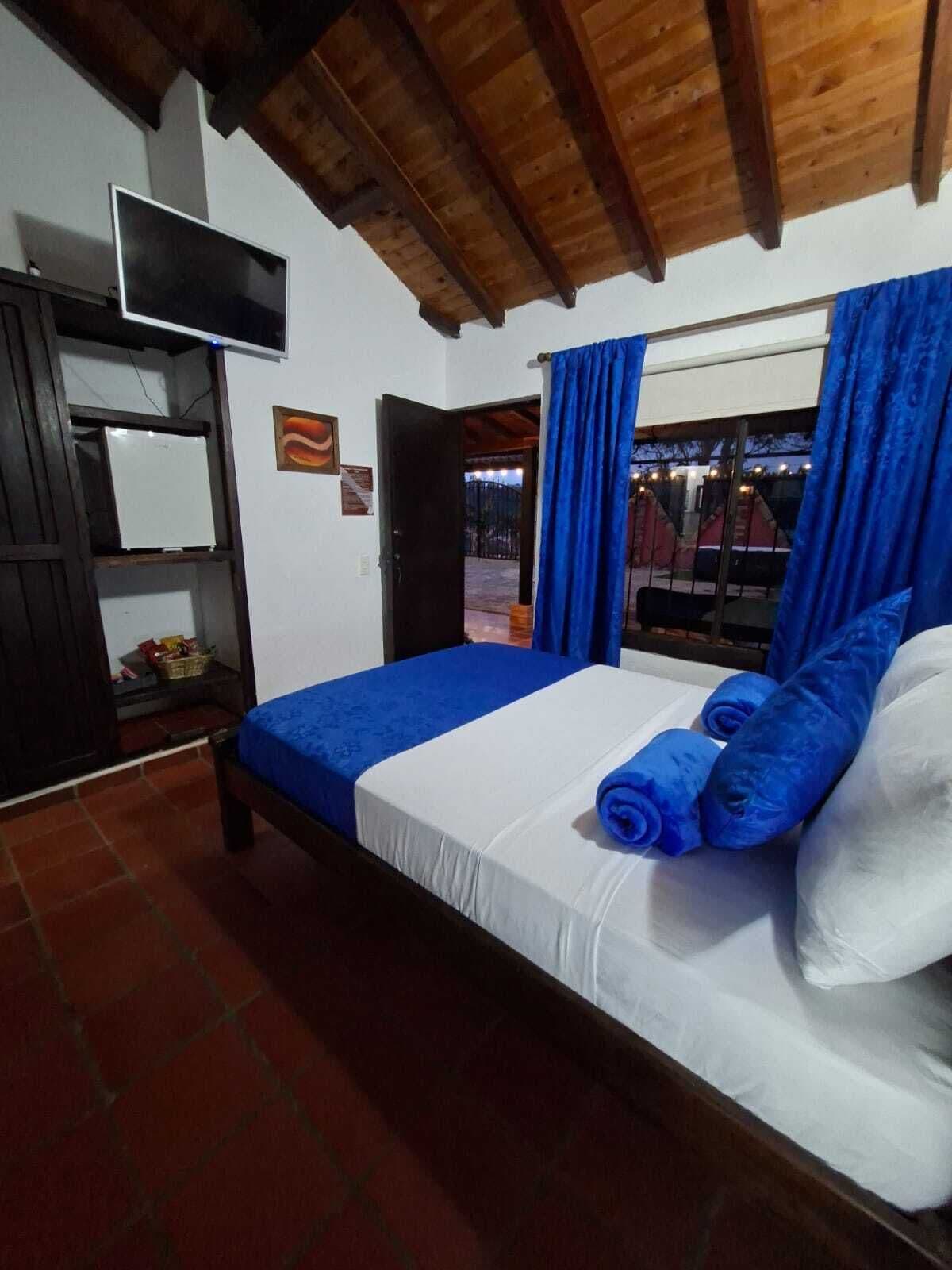 Quarto com cama, televisão, janela com cortinas e porta que dá para o exterior.