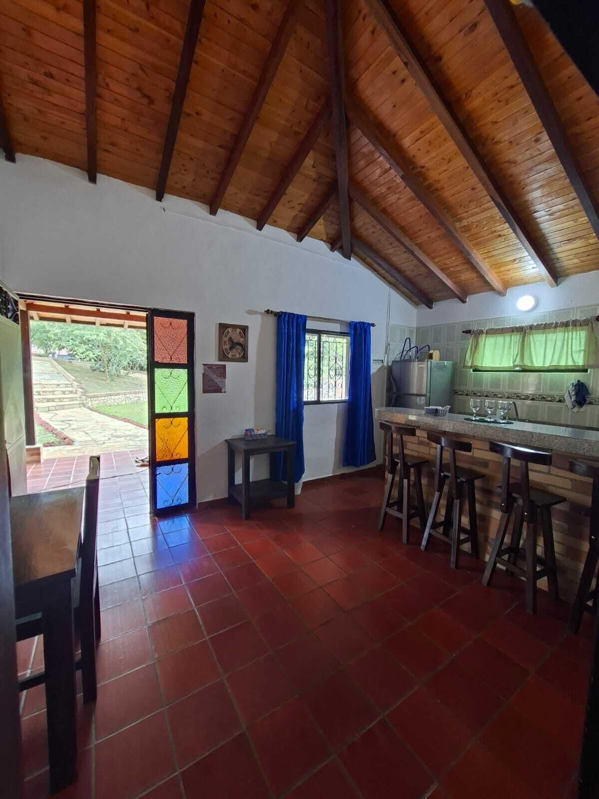 Una cocina con techo de madera, una zona de comedor con mesa y sillas, y vistas al exterior.