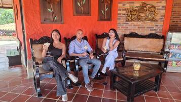 A group of people seated on wooden benches with a tiled floor, a small table with a drink, and decorative wall art.