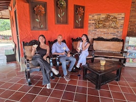 Un grupo de personas sentadas en bancos de madera sobre un piso de baldosas, una pequeña mesa con una bebida y decoración en las paredes.
