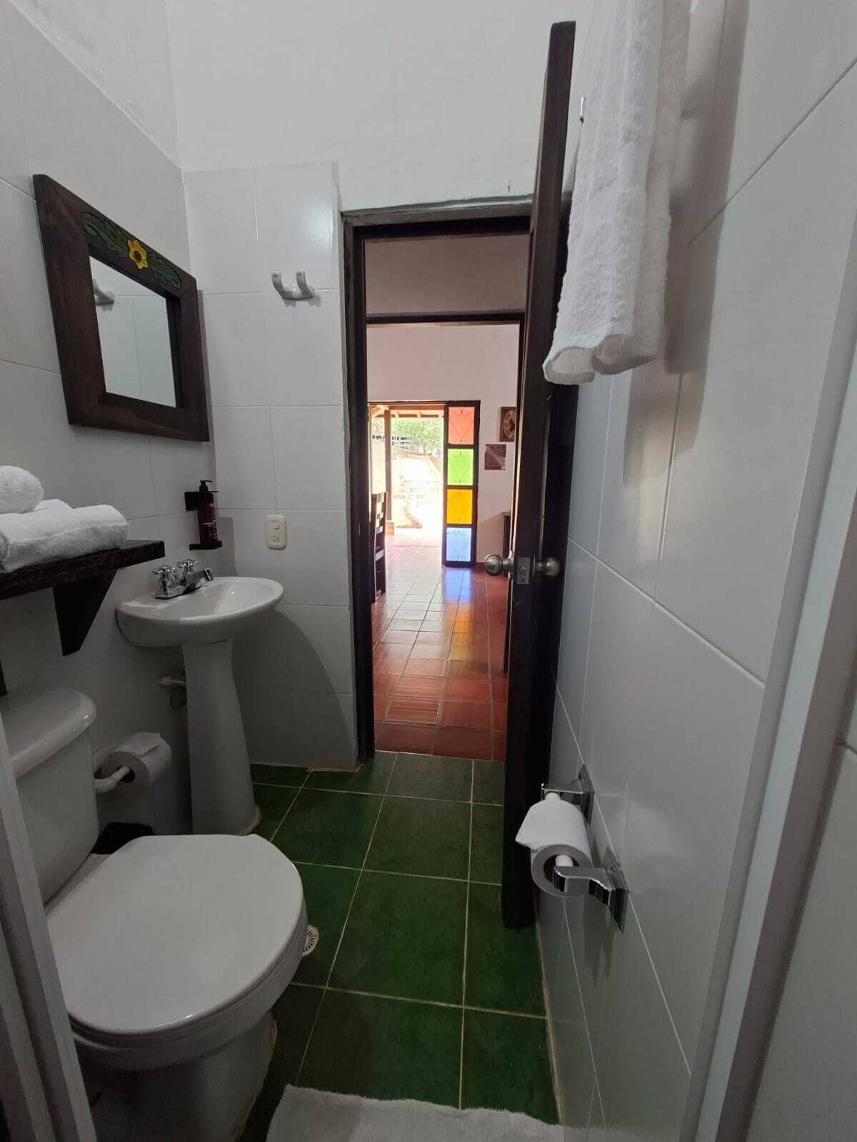 Et badeværelse med toilet, vask og spejl. Der hænger et håndklæde på væggen.