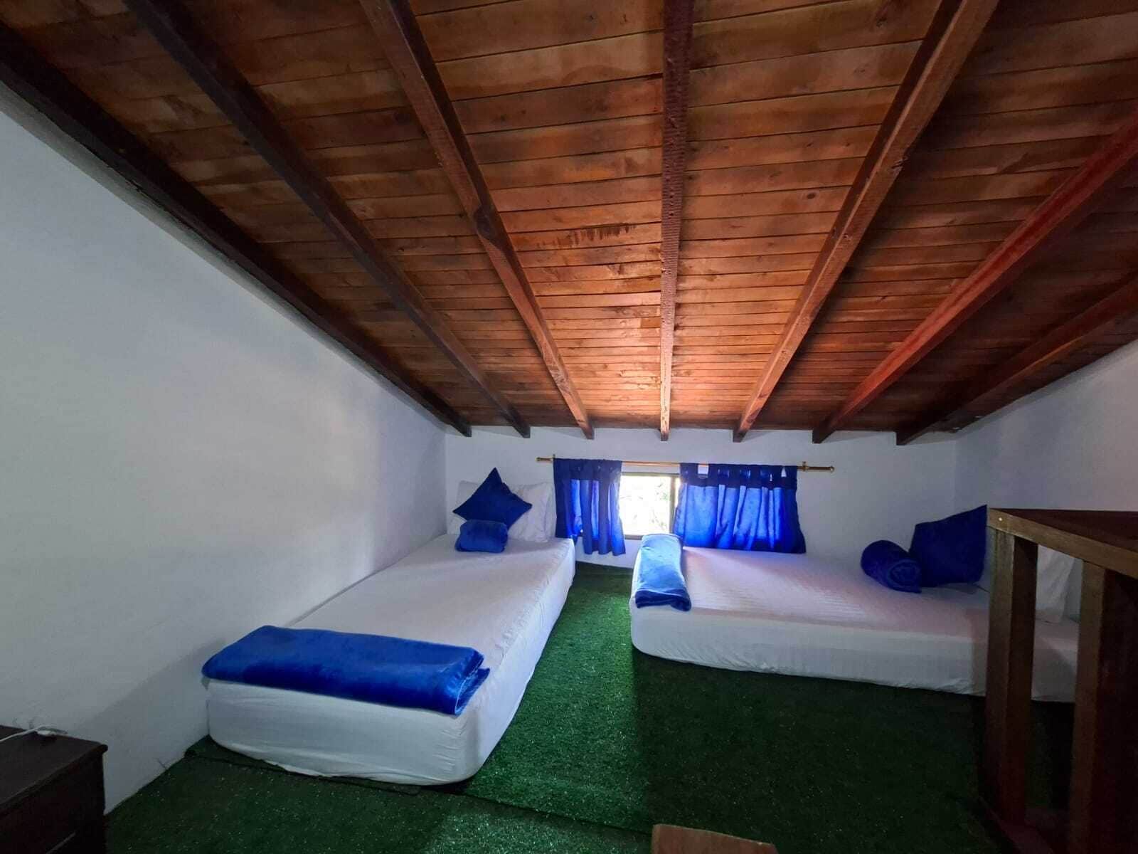 Quarto com duas camas, teto de madeira e janela com cortinas.