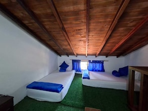 Una habitación con dos camas, techo de madera y ventana con cortinas.
