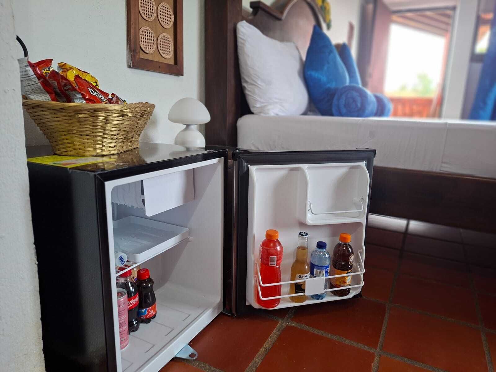 Un refrigerador compacto con una cesta de bocadillos, una botella de Coca-Cola y una botella de agua.
