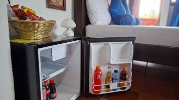 Un refrigerador compacto con una cesta de bocadillos, una botella de Coca-Cola y una botella de agua.