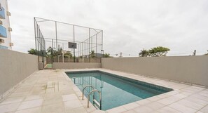 A swimming pool with a metal safety fence, a basketball court, and a basketball hoop. - Apartamento no Guaruja a 800m da Praia da Enseada (Guarujá)