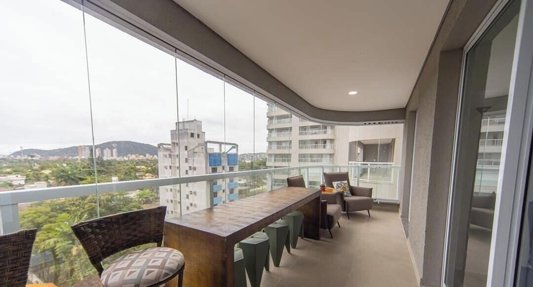 A balcony with a dining table and chairs, a view of the cityscape, and a glass railing.