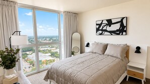 A hotel room with a large bed, a bedside table, a lamp, a mirror, and a view of the city. - Lovely 1-bedroom apartment with AC in Fort Myers (Fort Myers)