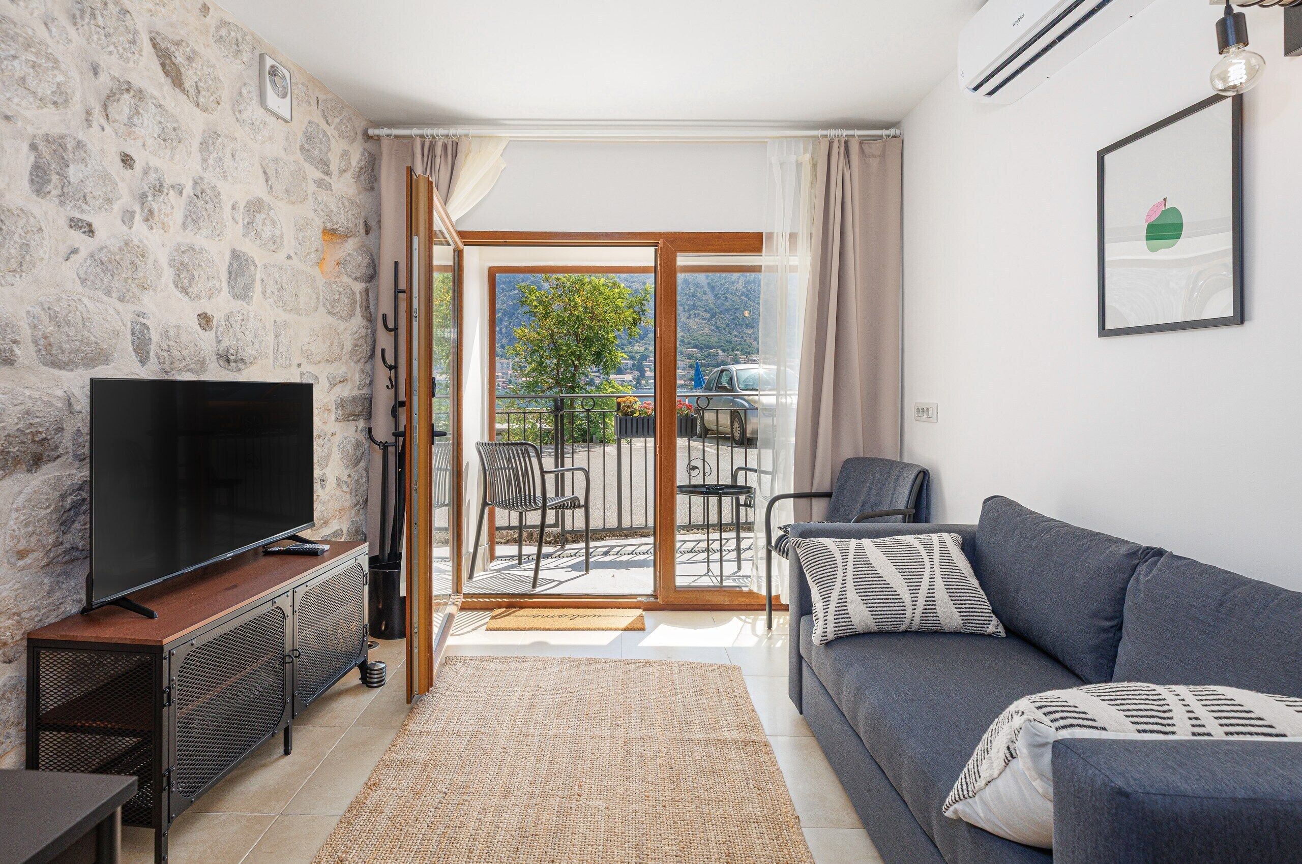 Una sala de estar con pared de piedra, televisor de pantalla plana, sofá gris y balcón con vistas.