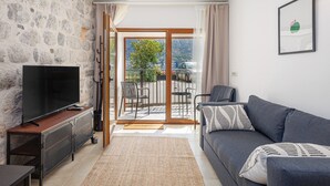 Un salon avec un mur en pierre, un téléviseur à écran plat, un canapé gris et un balcon avec vue.