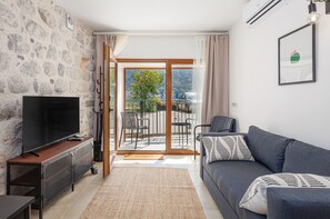 Ein Wohnzimmer mit Steinsäule, einem Flachbildfernseher, einem grauen Sofa und einem Balkon mit Blick.