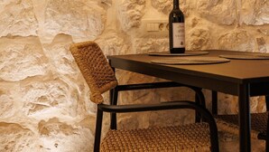 Un mur de pierres, une table avec une bouteille et des chaises en osier.