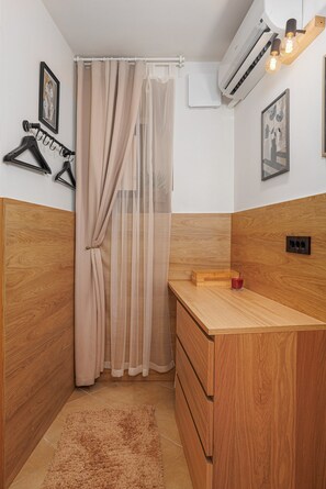 Ein kleiner, kompakter Raum mit einem Holzschrank, einem kleinen Holztisch, einem Spiegel und einer Wand-Klimaanlage.