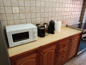 Una cucina con un forno a microonde bianco, una macchina da caffè e un rotolo di carta assorbente sul bancone.
