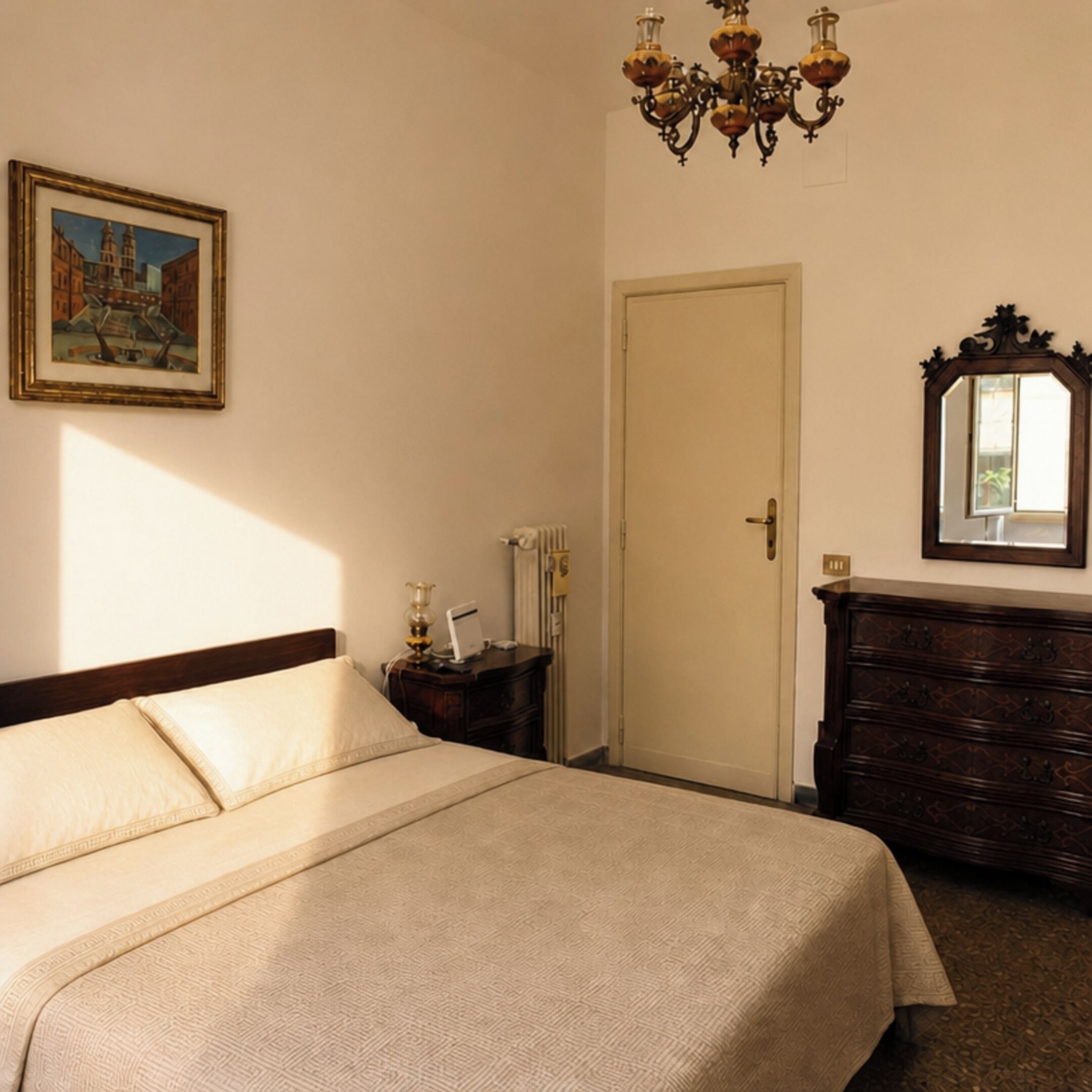 Habitación de hotel con cama, cómoda, espejo, candelabro, cuadro y puerta.