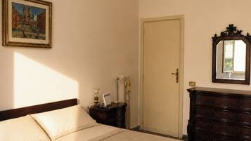 Habitación de hotel con cama, cómoda, espejo, candelabro, cuadro y puerta.