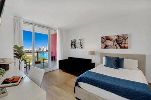 A modern hotel room with a bed, a desk, and a view of the cityscape through large windows. - Sky Views 2BR Intracoastal (Hallandale Beach)