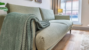 Ein grünes Sofa mit einer Decke, ein kleiner Tisch mit einer Lampe und ein Fenster mit Vorhängen.