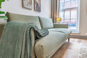 Ein grünes Sofa mit einer Decke, ein kleiner Tisch mit einer Lampe und ein Fenster mit Vorhängen.