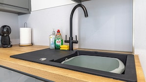 Eine Spüle mit Armatur, eine Kaffeemaschine und Reinigungsmittel auf der Arbeitsplatte.