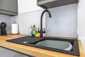 Eine Spüle mit Armatur, eine Kaffeemaschine und Reinigungsmittel auf der Arbeitsplatte.