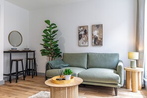 Un salon avec un canapé, une table basse, une plante et des œuvres d’art accrochées au mur.