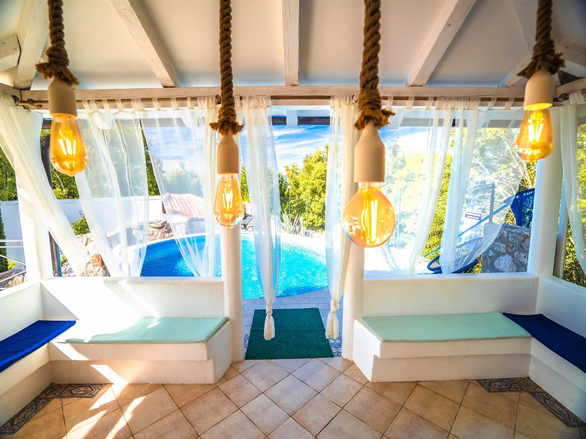 Une pièce lumineuse donnant sur la piscine, agrémentée de luminaires suspendus et de sièges confortables.