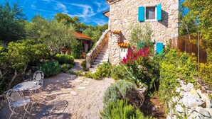 Uma casa de pedra com uma escadaria, um jardim com diversas plantas e área de estar ao ar livre.