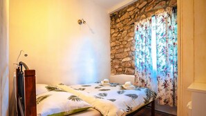 Um quarto pequeno e acolhedor com uma cama de solteiro, uma parede de pedra e uma janela com cortinas florais.
