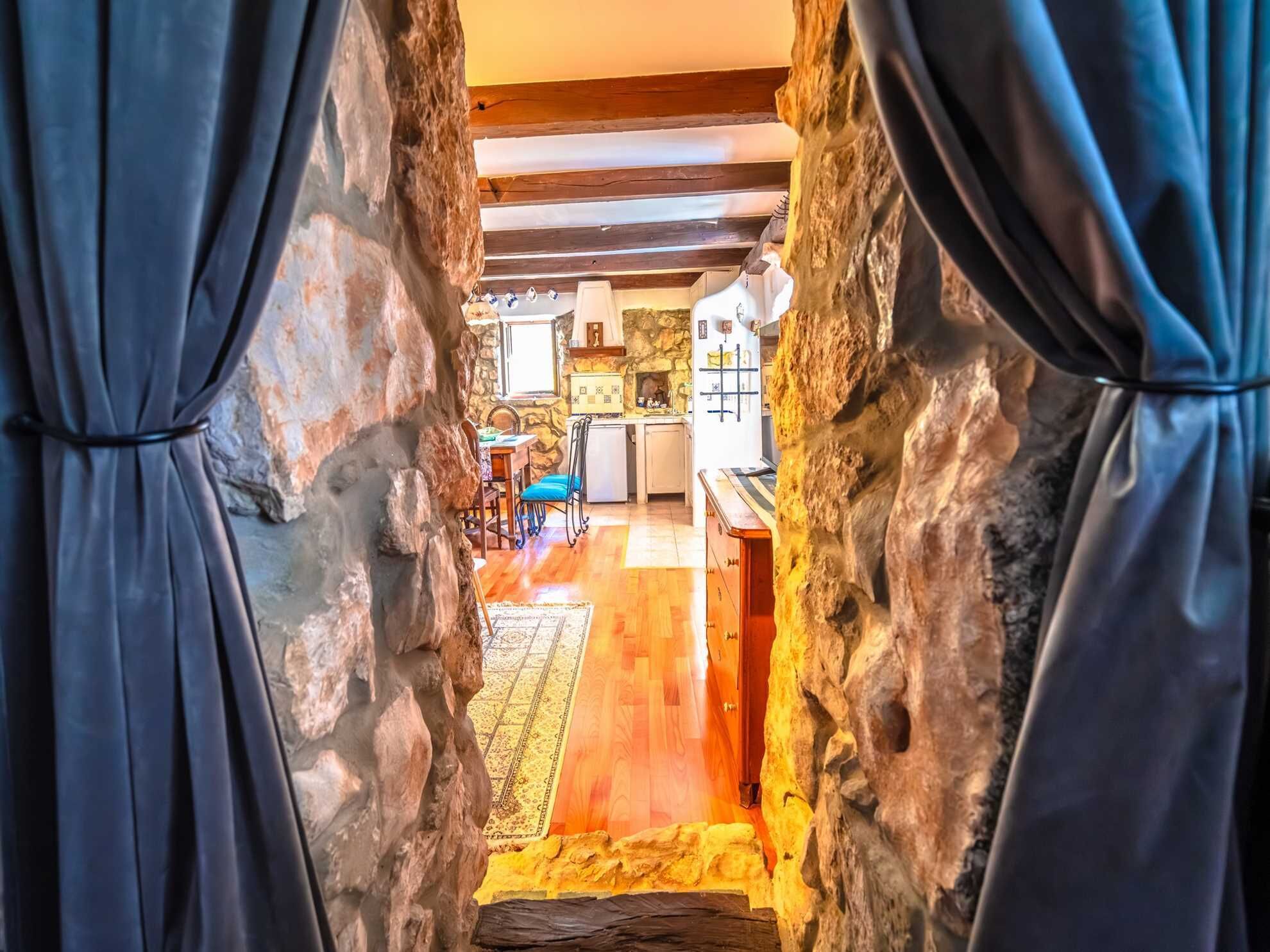 A narrow stone corridor leading to a kitchen with wooden flooring and a dining area.