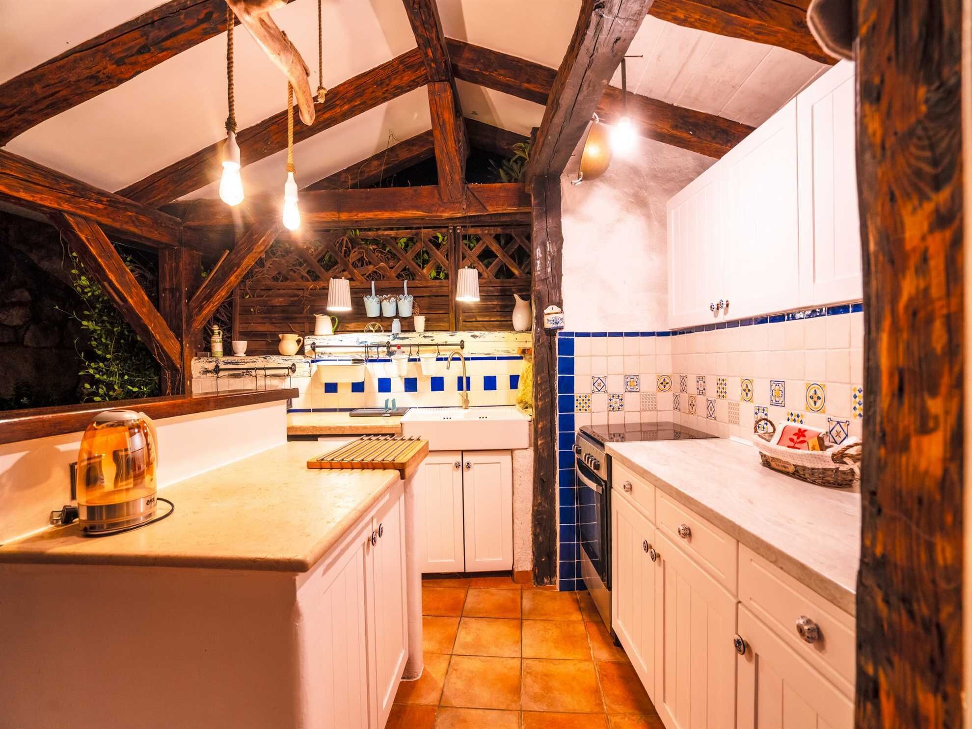 A rustic kitchen with exposed wooden beams, a tiled backsplash, and hanging pendant lights.