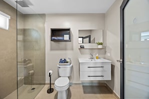 Een moderne badkamer met een glazen douchecabine, toilet, wastafel met spiegel erboven en een klein plankje met toiletartikelen.