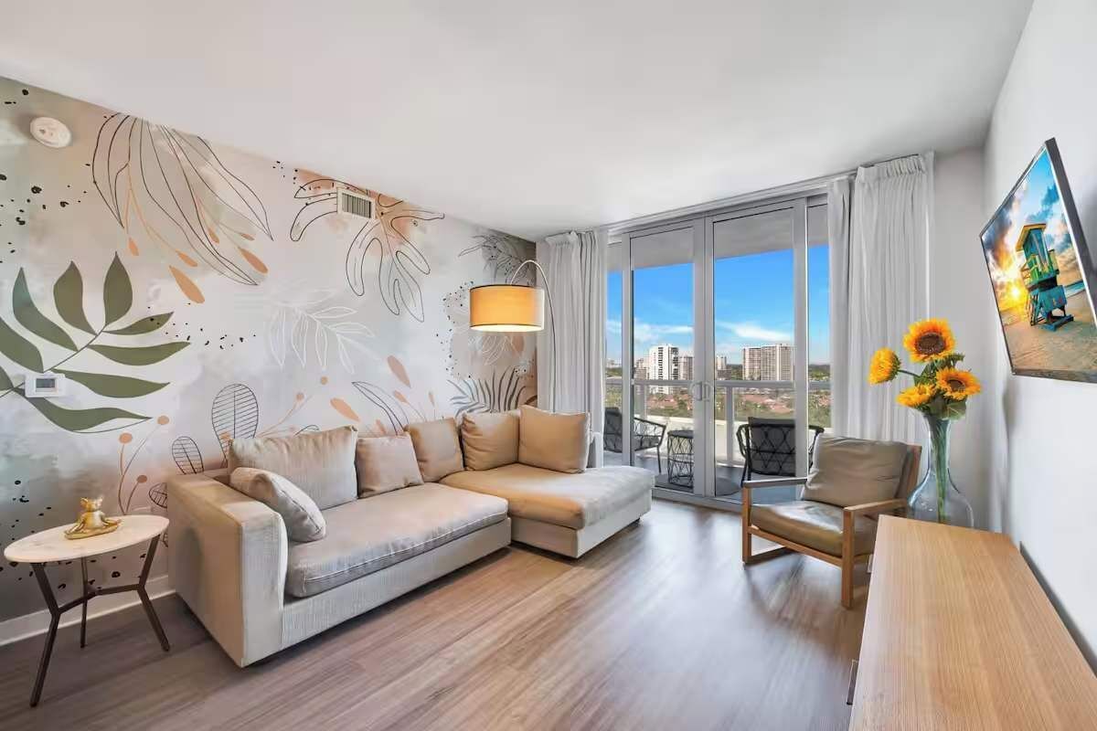 A modern living room with a sectional sofa, a small round table, a chair, and a large window with a city view.