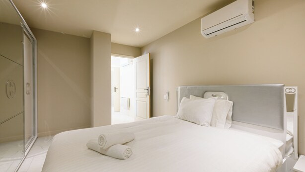 Une chambre d’hôtel comprenant un lit, une table de chevet, un appareil de climatisation et une porte donnant sur une autre pièce.