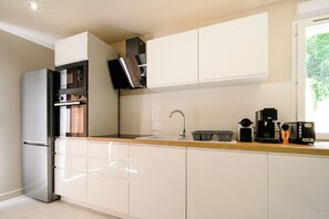 Eine moderne Küche mit weißen Schränken, einem Edelstahl-Kühlschrank, einem eingebauten Backofen, einer Kaffeemaschine und einem Fenster für natürliches Licht.