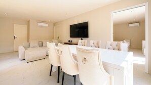 Un salon moderne comprenant un canapé, une table à manger avec des chaises, un téléviseur à écran plat fixé au mur et un appareil de climatisation.