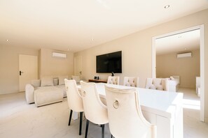 Ein modernes Wohnzimmer mit einer Couch, einem Esstisch mit Stühlen, einem an der Wand befestigten Flachbildfernseher und einer Klimaanlage.